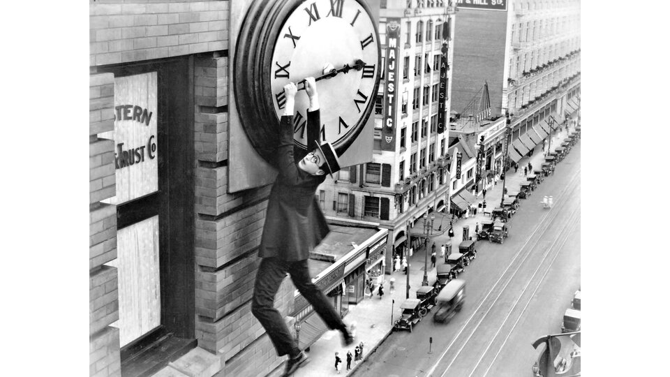 Schwarz-Weiss Foto mit einem Mann, der an einer Uhr in der Luft hängt.  | © Kultur am Pass